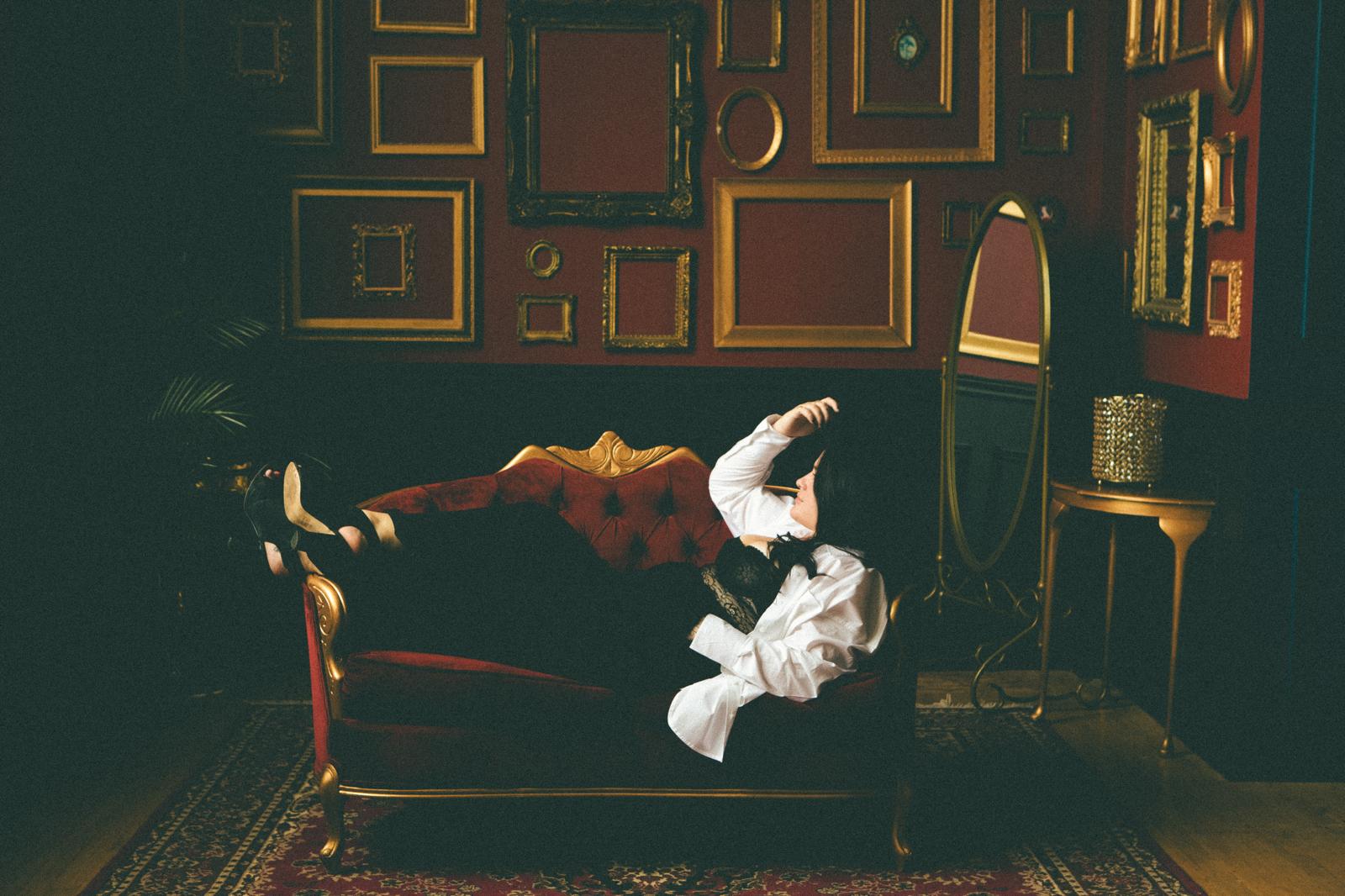 author lying across vintage couch, antique picture frames covering wall behind